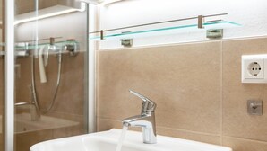 Ein Badezimmer mit einem weißen Waschbecken, einem Chrom-Wasserhahn und einer Glasablage darüber.