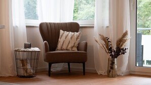 A corner room with a brown armchair, a small side table with a vase of dried plants, and a window with sheer curtains. - Apartment 'Wohnung Im Rheintal' with Balcony and Wi-Fi (Küssaberg)