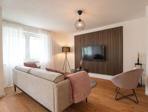 A living room with a sofa, a chair, a TV, a lamp, and a wall with vertical lines. - Apartment 'Wohnung Im Rheintal' with Balcony and Wi-Fi (Küssaberg)