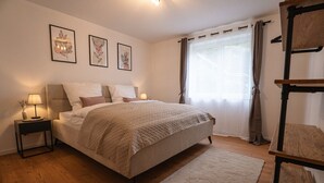 A bedroom with a bed, bedside tables, a lamp, a window with curtains, and wall art. - Apartment 'Wohnung Im Rheintal' with Balcony and Wi-Fi (Küssaberg)