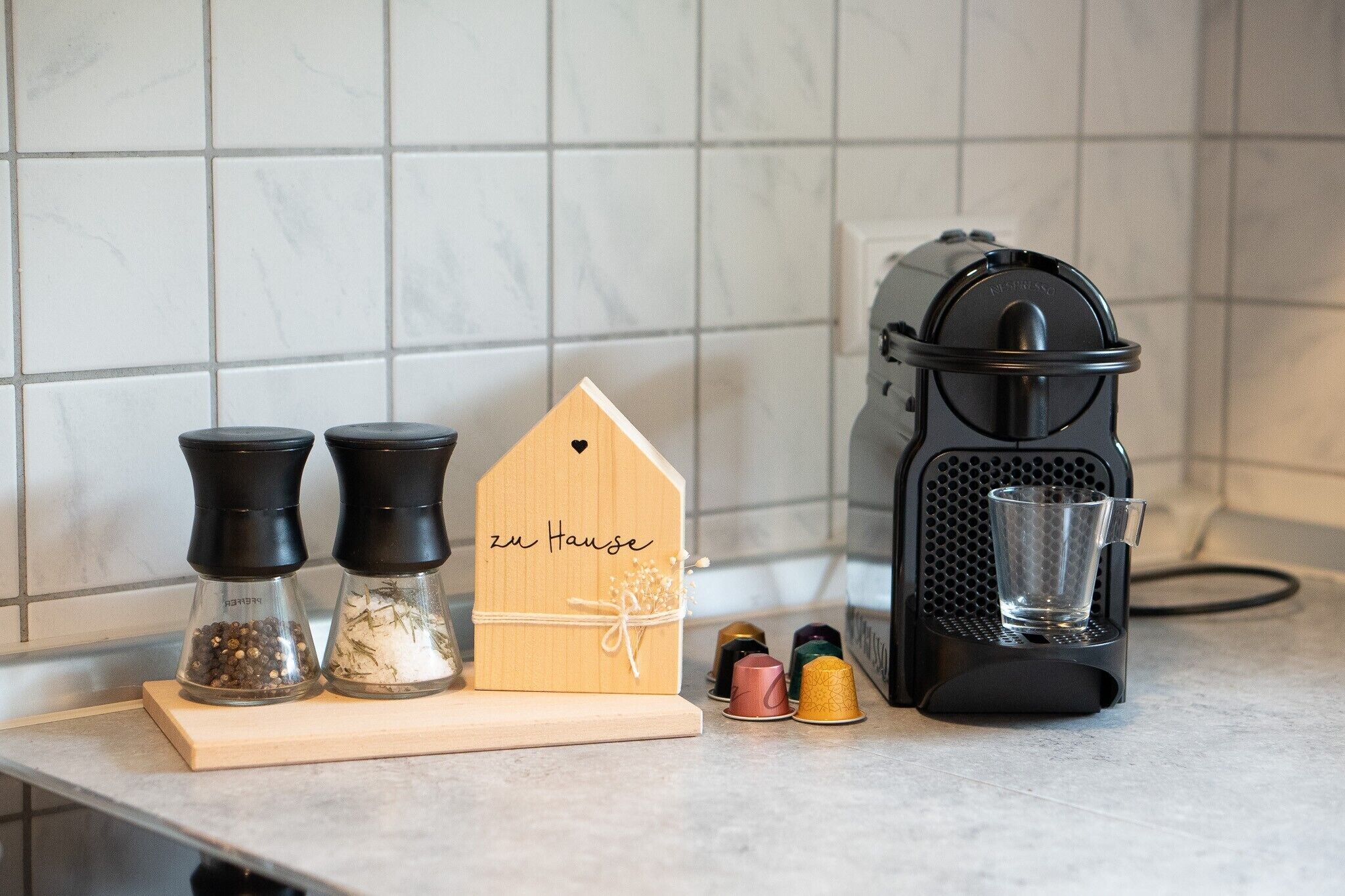 A kitchen counter with a coffee maker, pepper mills, and a wooden sign.