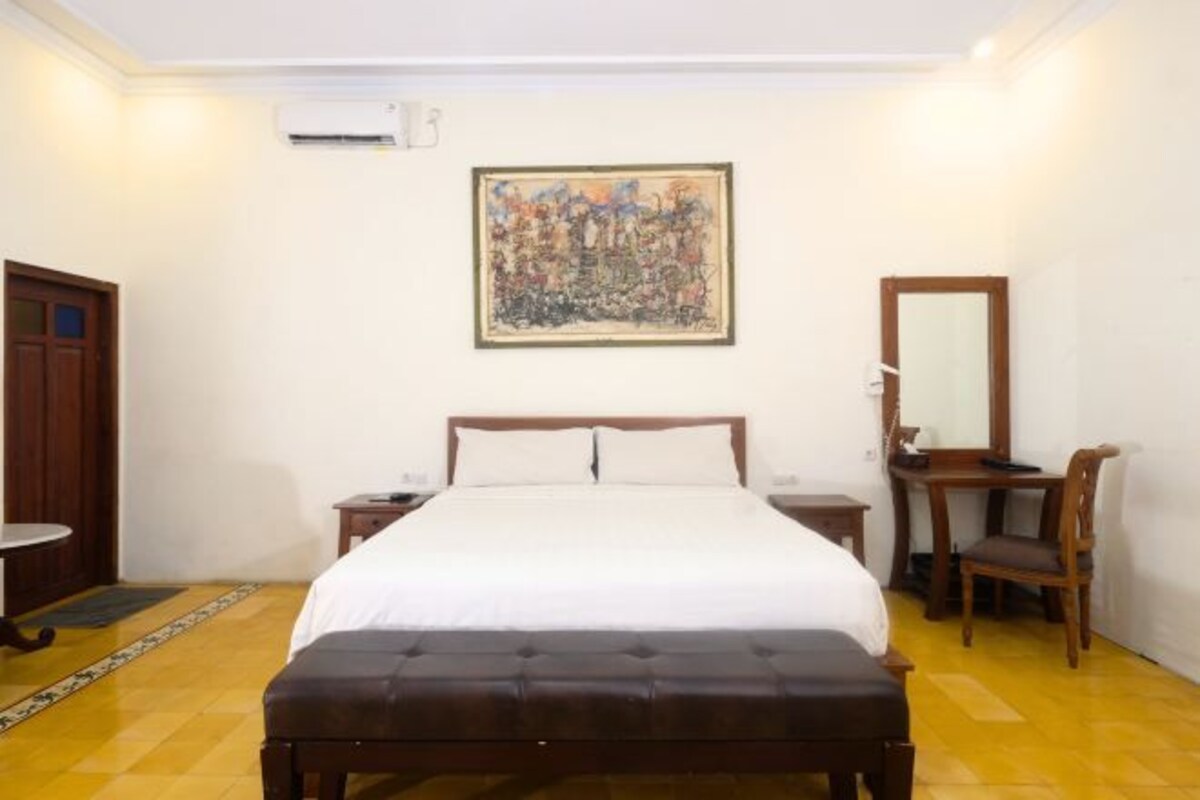A bedroom with a bed, a desk, a chair, a mirror, and a painting on the wall.