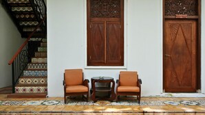 A staircase with ornate railings, two leather chairs, a small table, and a wooden door with intricate carvings. - The Mangkoro Hotel by Sinergi (Banguntapan)