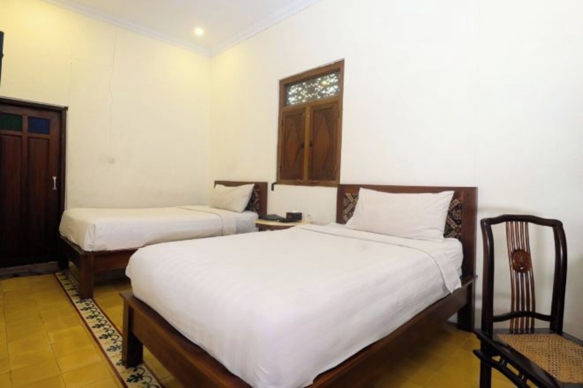 A room with two single beds, a wooden wardrobe, a chair, and a window with a decorative design.