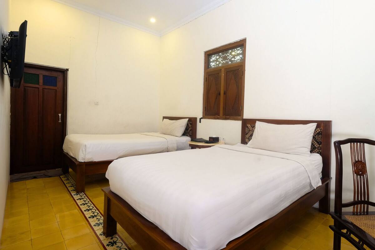 A room with two single beds, a wooden wardrobe, a chair, and a small table.
