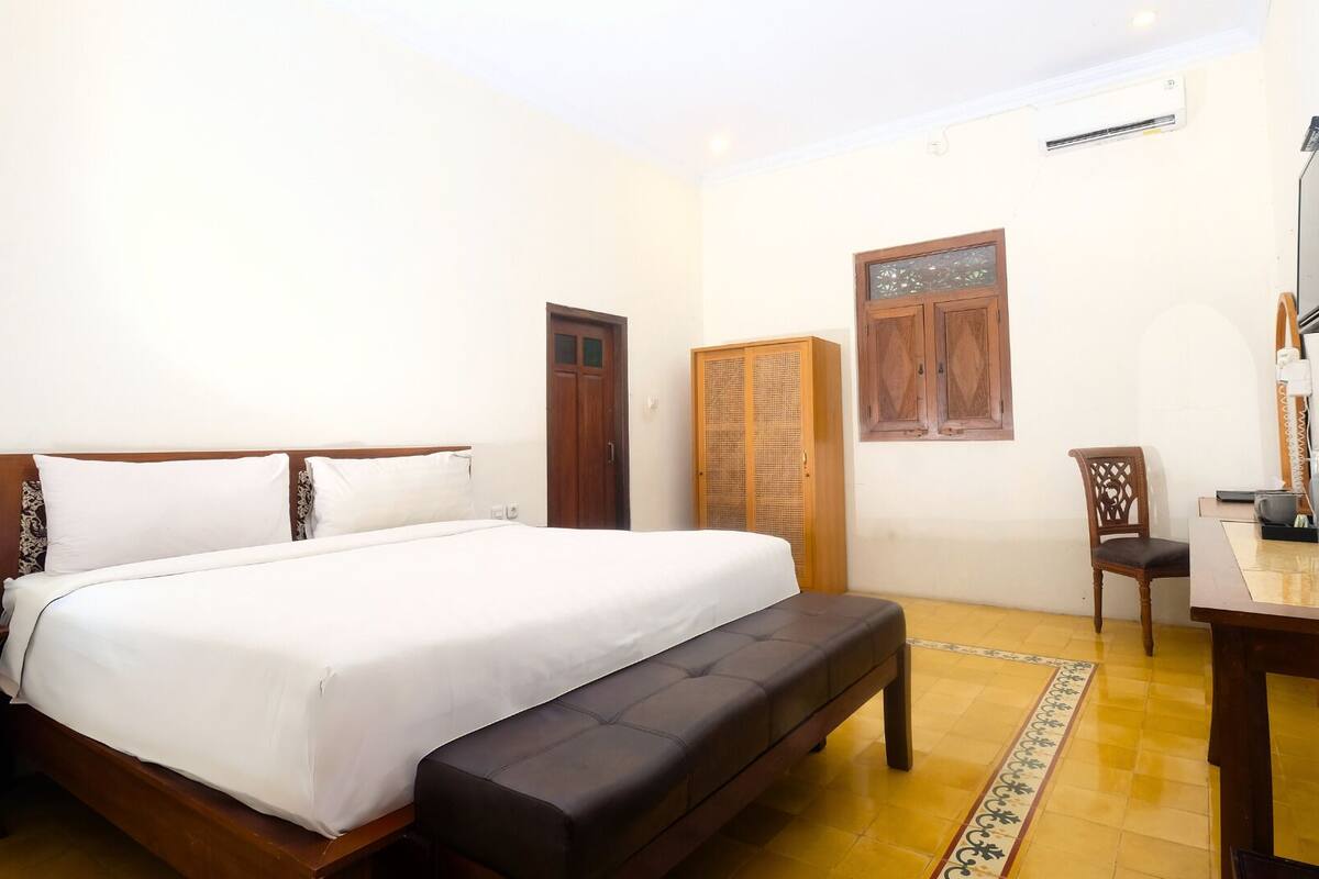 A bedroom with a bed, bench, wardrobe, chair, desk, and TV.
