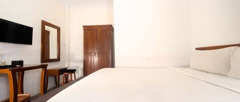 Une chambre d’hôtel avec un grand lit, un bureau en bois avec une chaise, un téléviseur à écran plat fixé au mur et une armoire en bois.