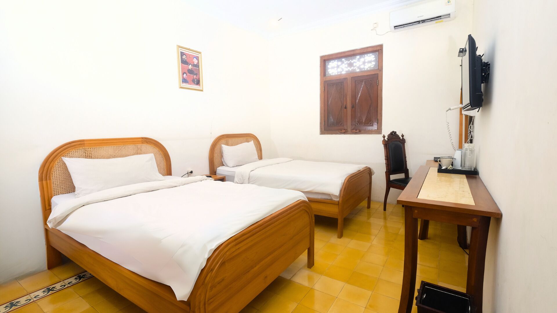 A room with two wooden beds, a desk, a chair, a window, and an air conditioning unit.