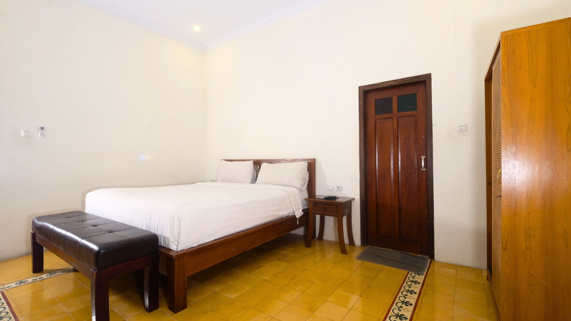 A bedroom with a wooden bed, a bedside table, a bench, and a wardrobe.