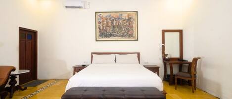 Una habitación de hotel con una cama, un escritorio, una silla, una mesita y un cuadro en la pared.