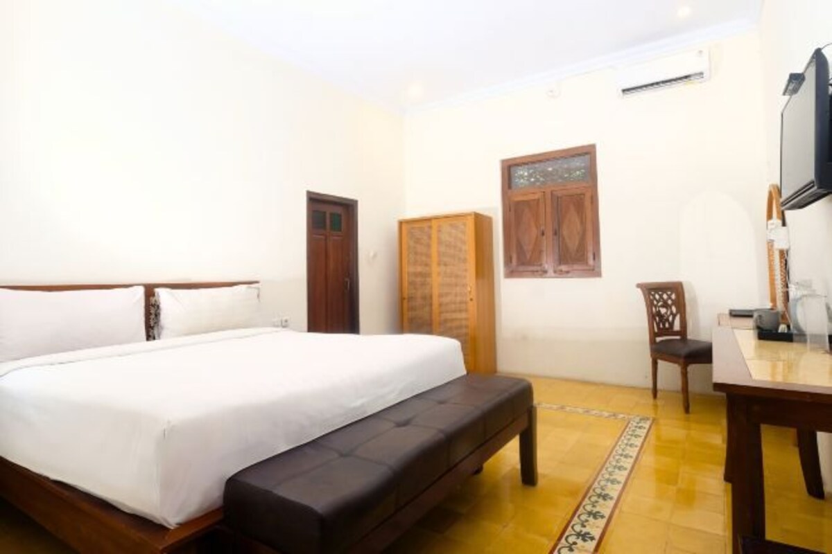 A bedroom with a bed, a wooden wardrobe, a chair, and a television.