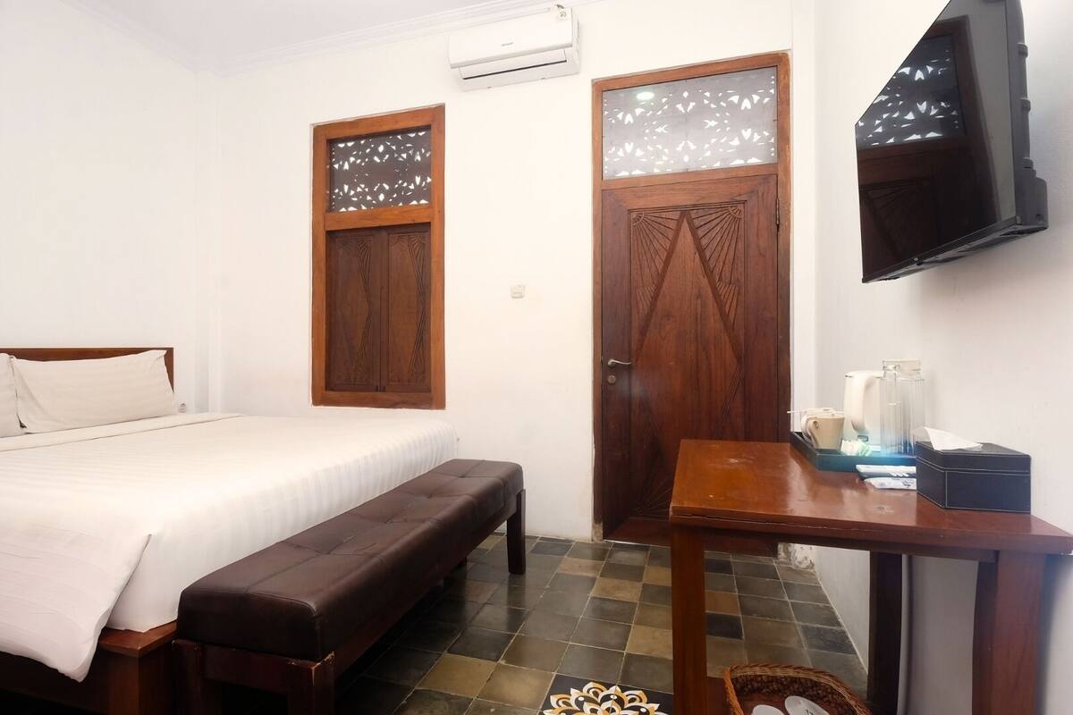A bedroom with a bed, a bench, a desk with toiletries, and a TV on the wall.