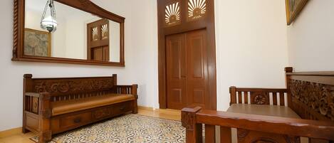 A room with a wooden bench, a dining table, a patterned rug, a large mirror, and a door with decorative cutouts.