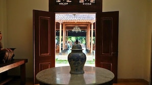 A traditional room with a round table in the center, a wooden door leading to an outdoor area, and a tiled floor. - The Mangkoro Hotel by Sinergi (Banguntapan)