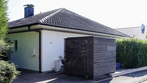 Un edificio moderno con tetto spiovente, una piccola struttura adiacente con facciata in metallo e un'area d'ingresso pavimentata.
