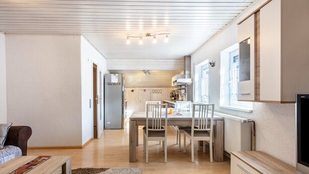 Una cocina moderna con armarios de madera, una mesa de comedor y sillas. Hay un refrigerador, un microondas y una ventana que proporciona luz natural.