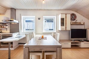 Uma cozinha moderna com mesa de jantar, cadeiras, televisão e um relógio na parede.