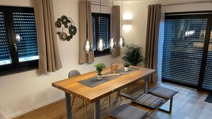 Un comedor con una mesa de madera, asientos tipo banco, lámparas colgantes y una planta en maceta.