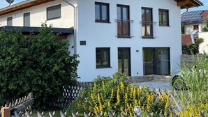 Una casa moderna de dos pisos con fachada blanca, varias ventanas y un balcón visible.