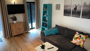 Una sala de estar con un sofá, una mesa de centro, un televisor, una estantería y una puerta que da a un balcón.