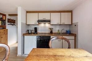 Une cuisine compacte avec des meubles blancs, un lave-vaisselle, une cuisinière et une table à manger en bois.