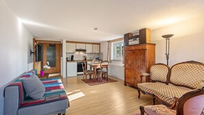 Een woonkamer met een bank, een houten kast en een eethoek met stoelen.