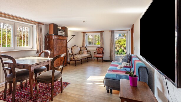 Een woonkamer met een eettafel, stoelen, banken, een televisie en uitzicht op de omgeving.