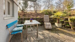 Een terras met een tafel, een bank, een stoel en planten in potten.