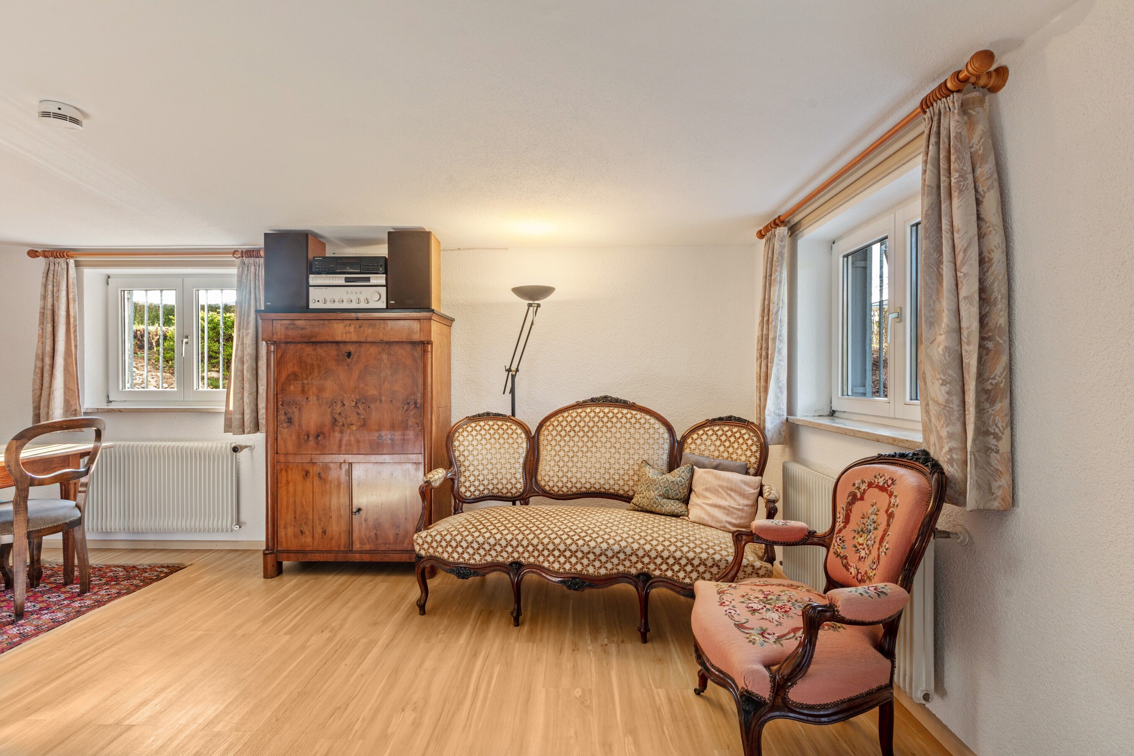 A living room with a wooden floor, a sofa, a chair, a cabinet, and a window with curtains.