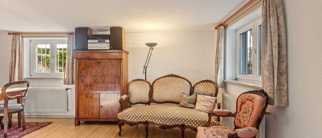 A living room with a wooden floor, a sofa, a chair, a cabinet, and a window with curtains.