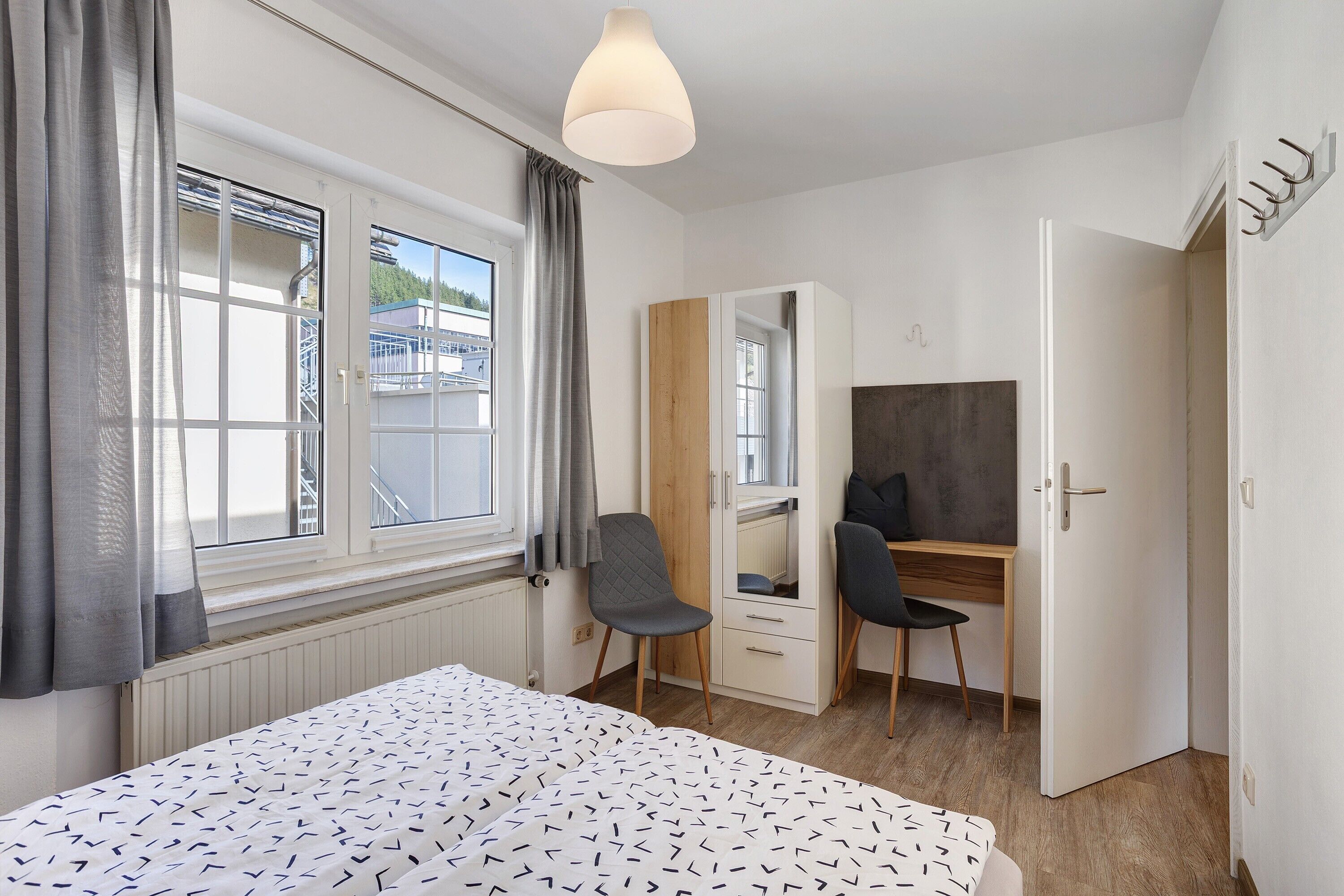 A bedroom with a bed, a desk, a chair, a wardrobe, and a window with curtains.