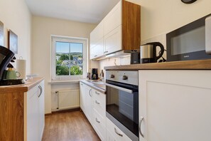 A compact kitchen with white cabinets, a built-in oven, a coffee maker, and a view through a window.