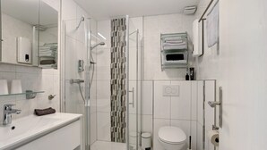 Une salle de bain moderne avec une douche à parois de verre, des toilettes blanches et un lavabo surmonté d’une plaque de verre.