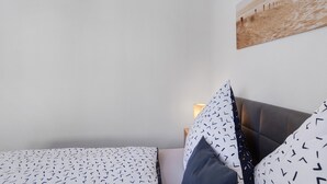 Makuuhuone, jossa on sänky, tyynyjä, seinään kiinnitetty valaisin ja taulu.