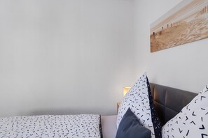 Een slaapkamer met een bed, kussens, een wandlamp en een schilderij.