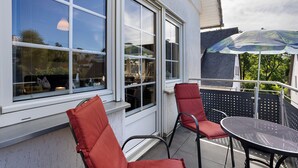 Un balcon avec une table et des chaises, de grandes fenêtres et une vue sur le ciel.