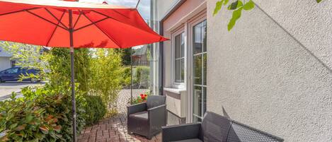 An outdoor seating area with a red umbrella, wicker furniture, and a view of the street.