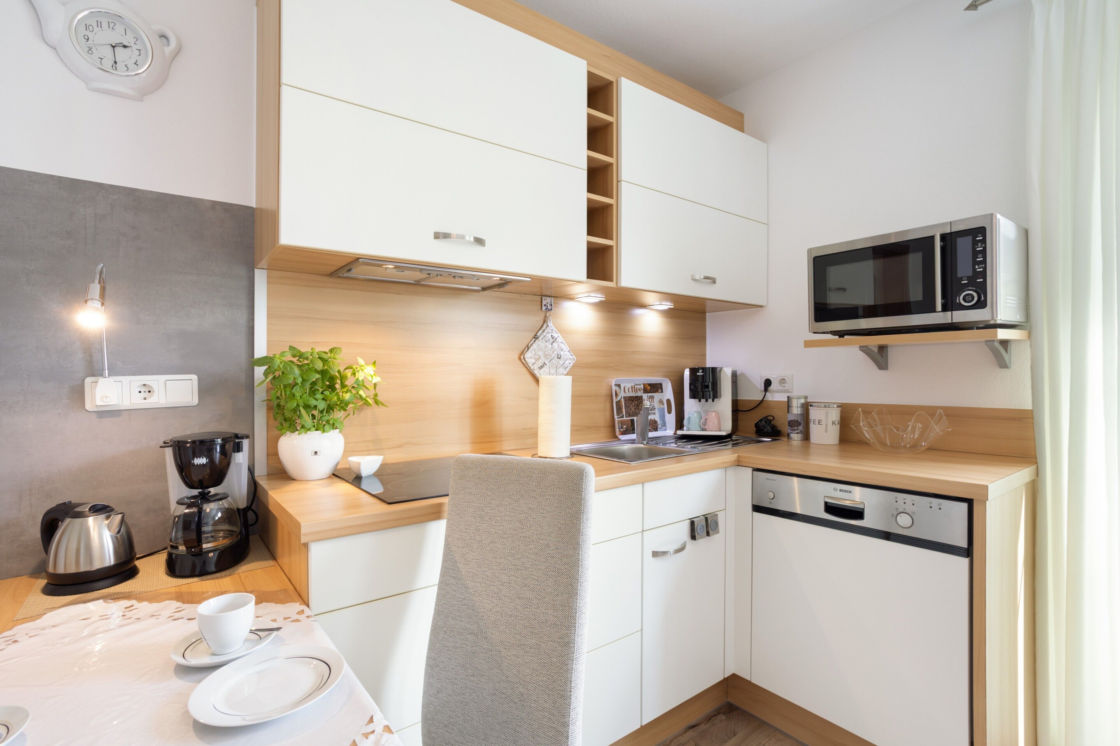 Een moderne keuken met witte kastjes, een magnetron, een koffieapparaat en een spoelbak.