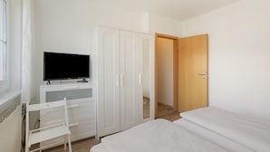 Une chambre à coucher avec un lit, un téléviseur posé sur un bureau, une chaise et une armoire.