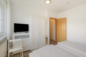 Quarto com cama, televisão sobre uma escrivaninha, uma cadeira e um guarda-roupa.