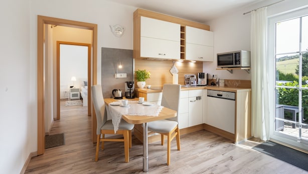 Une cuisine moderne avec un coin repas, des meubles en bois, un four à micro-ondes et une vue sur la verdure environnante.