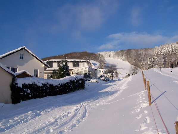 Un barrio residencial cubierto de nieve con casas, una pista de esquí y un cielo azul despejado.