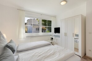 Un dormitorio con dos camas, televisor, armario y ventana con cortinas.