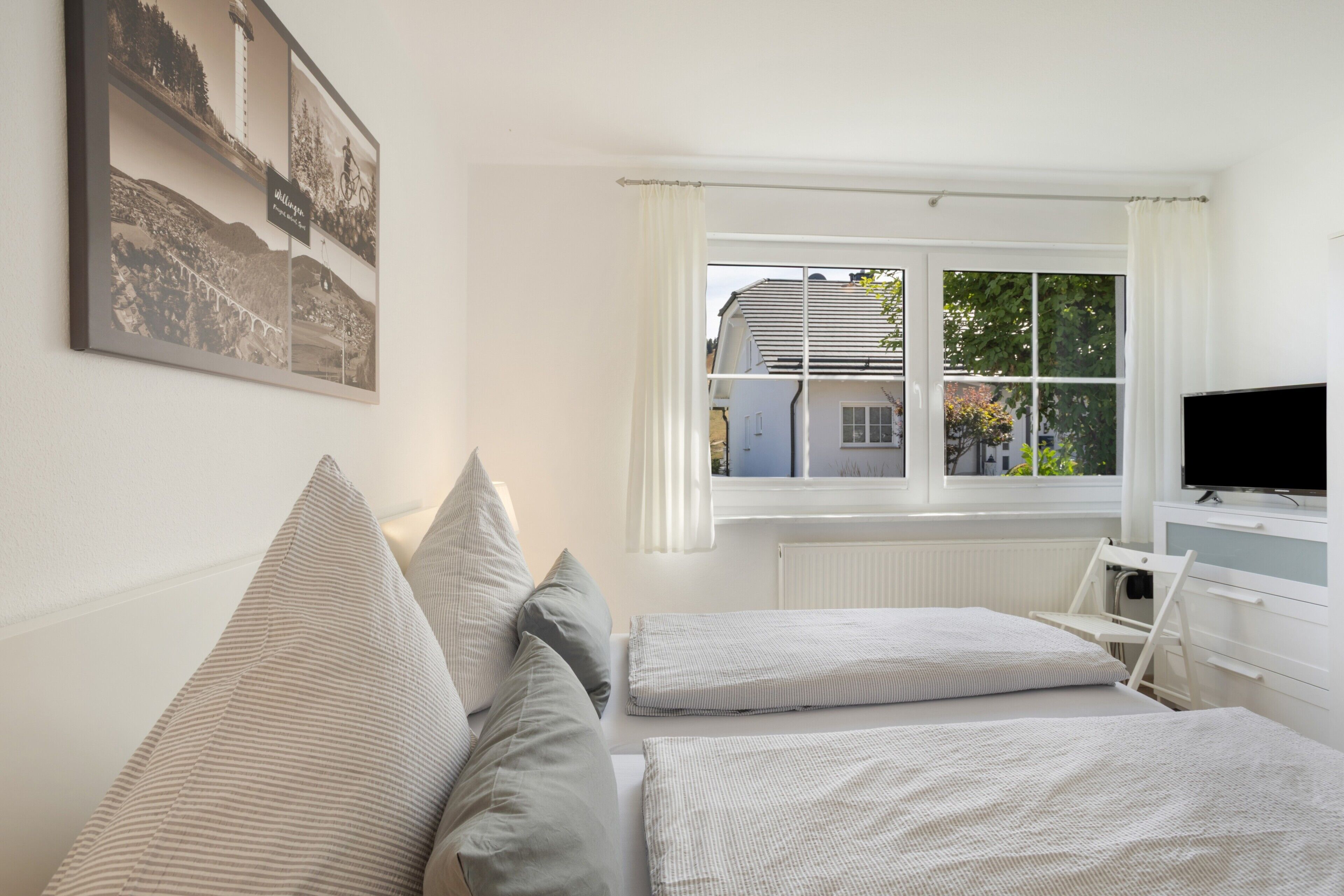 A bedroom with two beds, a window with curtains, a television, and a framed picture on the wall.