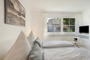 A bedroom with two beds, a window with curtains, a television, and a framed picture on the wall.