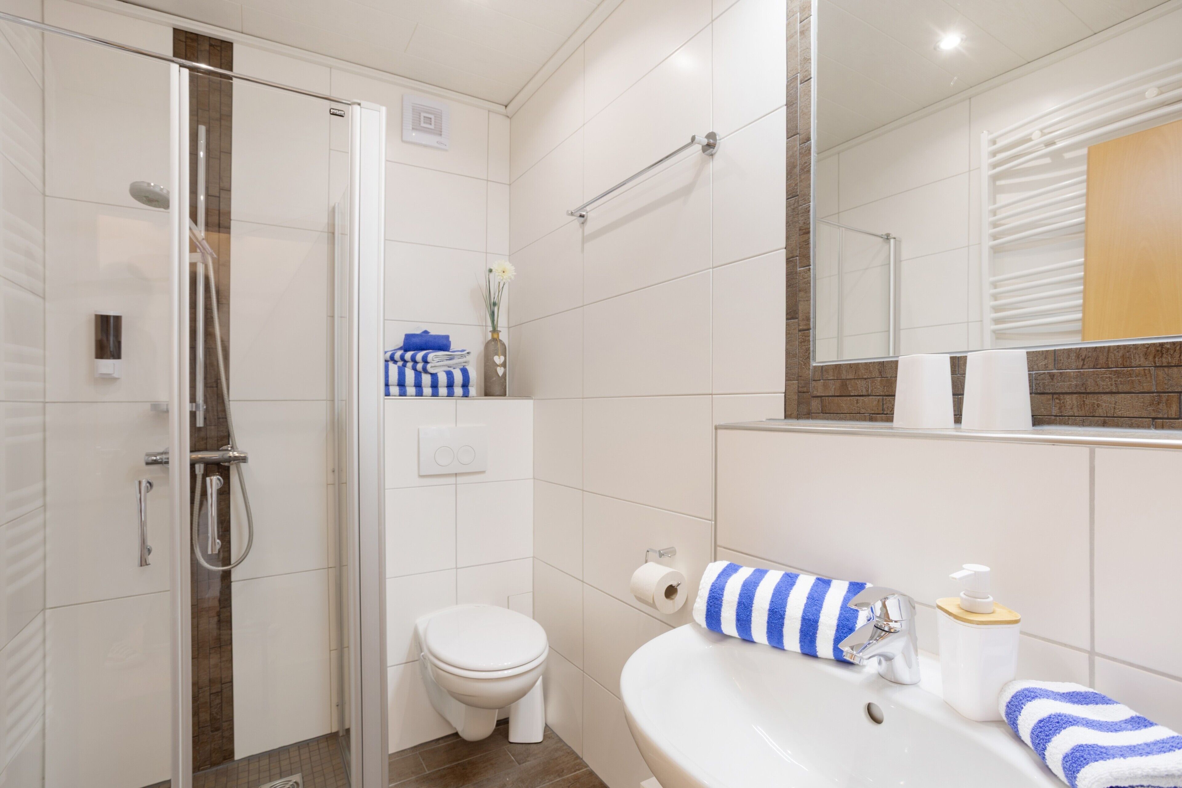 A modern bathroom with a glass-enclosed shower, a white toilet, and a sink with a mirror above it.