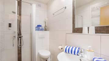 A modern bathroom with a glass-enclosed shower, a white toilet, and a sink with a mirror above it.