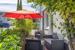 An outdoor patio area with wicker furniture and a red umbrella.
