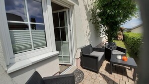 Une terrasse avec des meubles d’extérieur, une porte et une vue sur un bâtiment voisin.