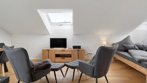 A modern loft bedroom with a skylight, a bed, a TV, and a desk area.